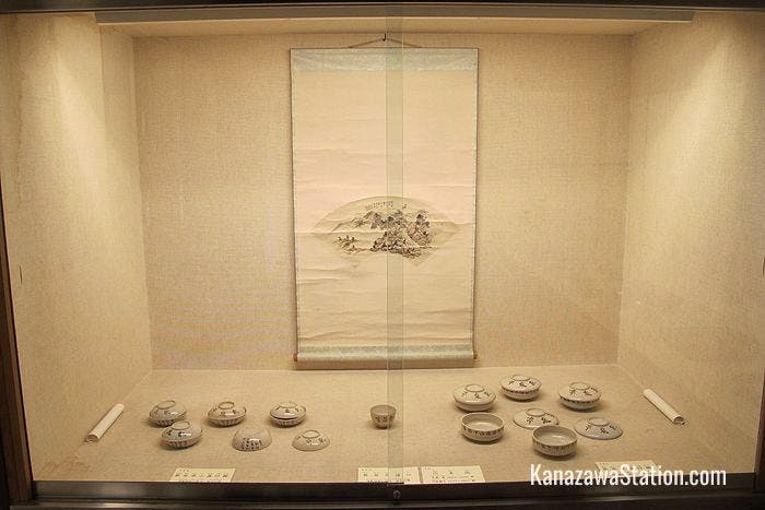 White porcelain bowls are displayed below a fan painting by the daughter of Kurando Terashima
